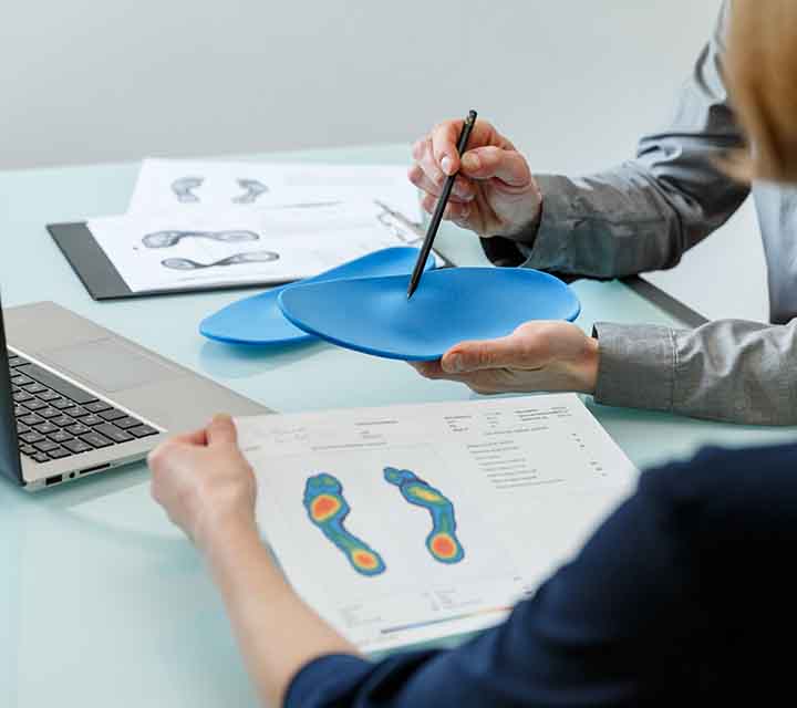 Foot pressure measurement charts are reviewed by client while orthotist holds orthotic insoles.