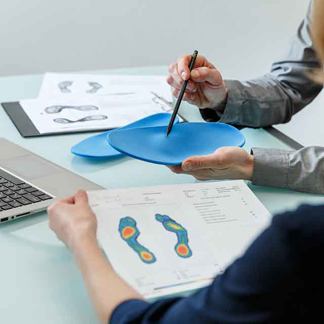 Client looking at printout of foot pressure measurements while orthotist demonstrates with a custom orthotic insert.